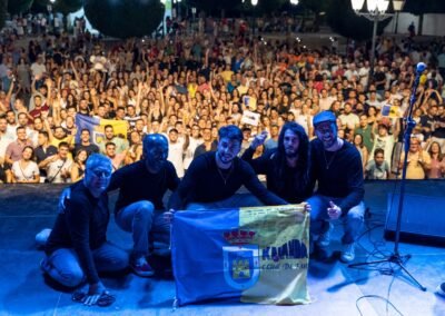 Grupo Kalanda posando en el escenario con el público y la bandera de su club de fans
