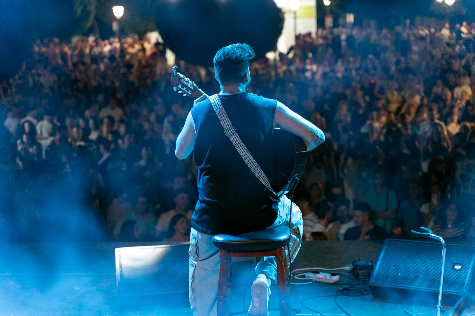 Blas Menchén tocando la guitarra de espaldas frente a una plaza llena de público