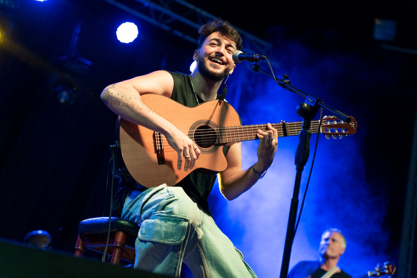 Blas Menchén sonriendo mientras canta y toca la guitarra en un concierto