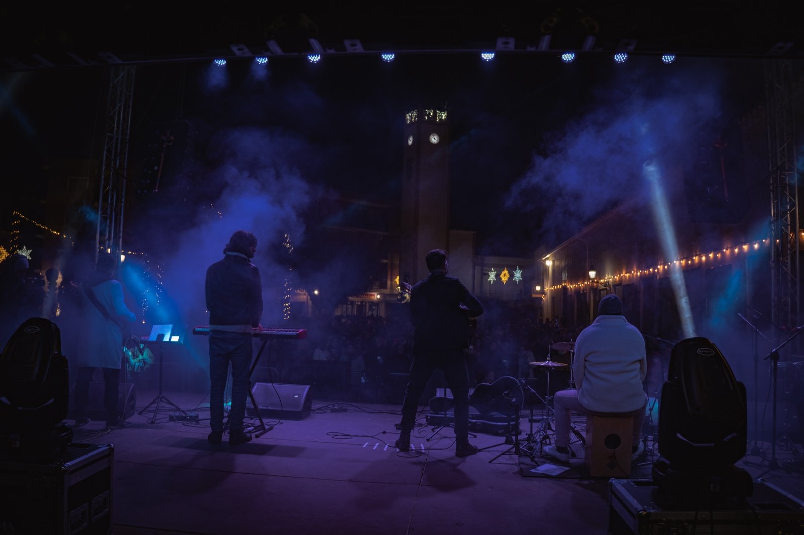 Grupo Kalanda tocando de espaldas frente a una plaza con un reloj iluminado